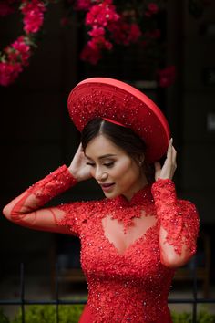 a woman in a red dress and hat poses for the camera with her hands on her head