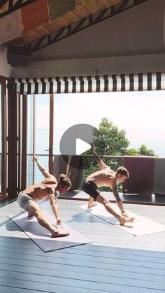 two men doing yoga on mats in front of an open window with the ocean behind them