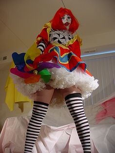 a woman dressed as a clown is standing on a bed