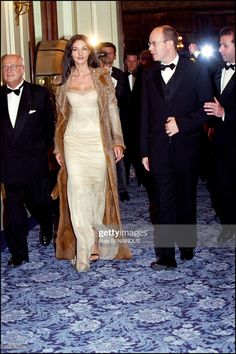 an elegantly dressed woman in a white dress and fur coat walks with other men