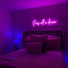 a bed with purple sheets and pillows in a room that has neon lights on the wall