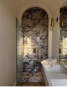 a bathroom with marbled walls and flooring in the shower area, along with two gold faucets