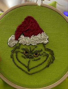 the grin face has been embroidered on to a green piece of fabric with a red santa hat