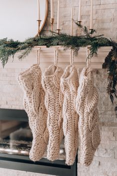 three knitted stockings hanging from a fireplace with pine needles and greenery on the mantle