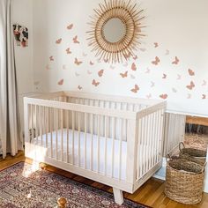 a white crib in front of a wall with butterflies on it and a mirror above the crib