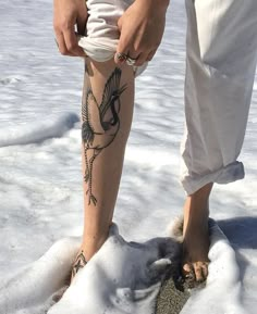 a person standing in the snow with tattoos on their legs and feet, while holding something in his hand