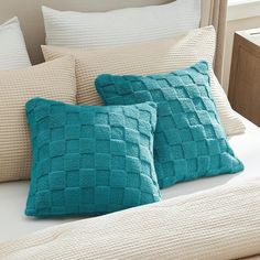 two teal colored pillows on a bed with white sheets and beige pillowcases