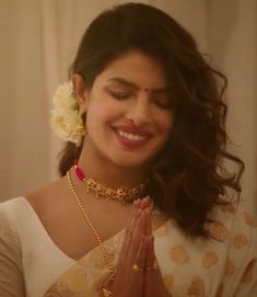 a woman wearing a white sari and smiling while holding her hands together in front of her face