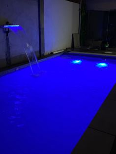 an empty swimming pool lit up with blue lights and water spouting from the side