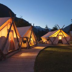 several tents are lit up at night in the mountains near a wooden walkway leading to them