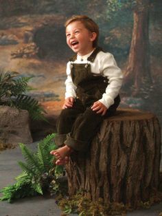 a young boy sitting on top of a tree stump in front of a forest scene