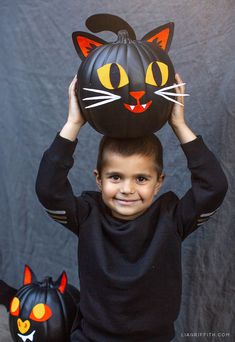 a young boy is holding up a pumpkin with a cat head on top of it