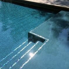 an empty swimming pool with clear blue water and sun reflecting on the glass flooring