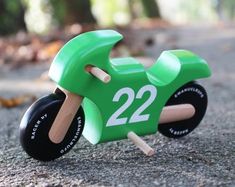 a green wooden toy motorcycle with numbers on the front and back wheels, sitting in the street