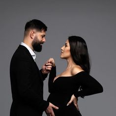 a man and woman standing next to each other in front of a gray background wearing black