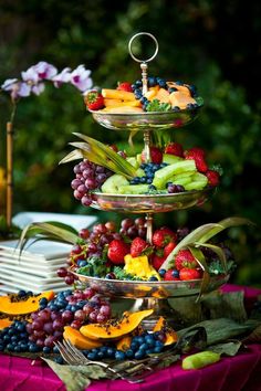 three tiered trays filled with fruit on top of a purple cloth covered table