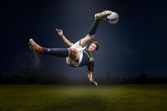 a man is kicking a soccer ball in the air on a field at night time