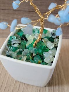 a white bowl filled with lots of green and blue glass beads on top of a wooden table