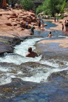 people are standing in the water near some rocks and boulders, while others stand around