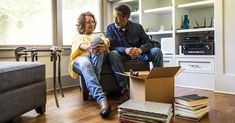 a man and woman sitting on a couch in front of a box filled with books