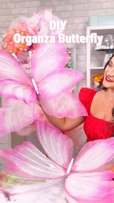 a woman in a red dress is holding pink butterfly wings and smiling at the camera