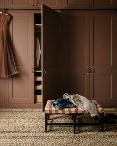 an open closet with clothes hanging on the wall and a bench in front of it