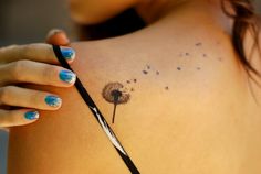 a woman holding a pair of scissors in her right hand while she has a dandelion tattoo on her left shoulder