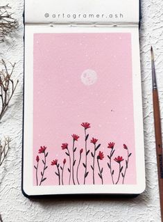 a pink card with red flowers on it next to a pencil and some dry grass