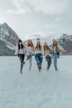 three girls are standing in the snow with their arms outstretched