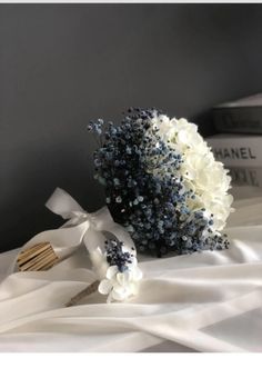 a bridal bouquet with blue and white flowers sits on a bed next to a stack of books