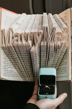 a person holding an open book with a ring in it's middle and the pages folded down