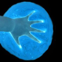 an image of a hand that is glowing in the dark blue light with water droplets on it