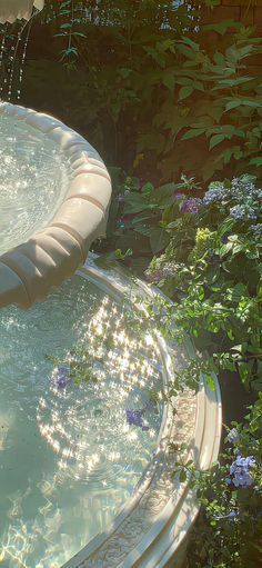 a water fountain in the middle of a garden with flowers and plants around it, surrounded by greenery