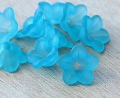 five blue flower beads sitting on top of a wooden table next to a cell phone