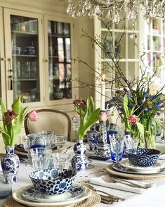 a dining room table set with blue and white dishes, vases filled with flowers