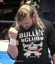 a man with long hair wearing a black shirt and holding his hand up to his face