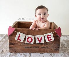 a baby sitting in a wooden crate with the word love spelled on it