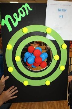 a person holding up a sign with balls in the center and neon green letters on it