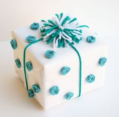 a white present box decorated with blue and white crocheted decorations, tied with green string