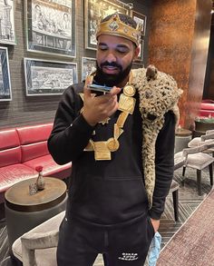 a man wearing a crown is looking at his cell phone in a room with pictures on the wall