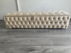 a white tufted bench sitting on top of a wooden floor next to a wall