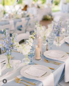 the table is set with white and blue flowers in vases, candles, and napkins