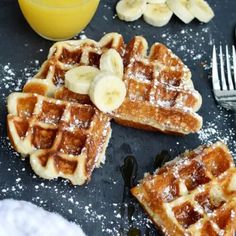 waffles with bananas and powdered sugar on a black plate next to a glass of orange juice