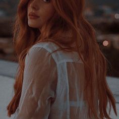 a woman with long red hair standing on top of a roof looking off into the distance