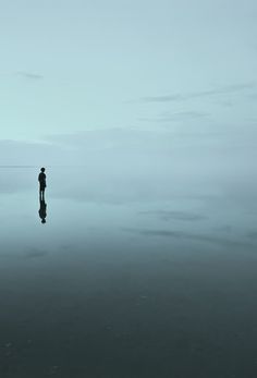 a lone person standing in the water on a foggy day