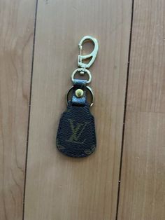 a louis vuitton keychain hanging on a wooden floor with a metal hook