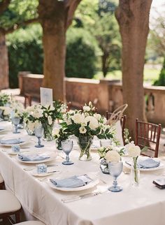 a wooden table topped with lots of white flowers and greenery next to silverware