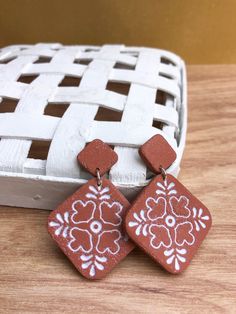 a pair of red and white earrings sitting on top of a wooden table next to a basket