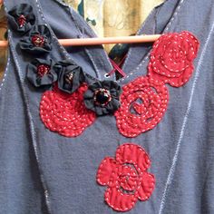 a blue shirt with red and black flowers on the front, attached to a wooden hanger