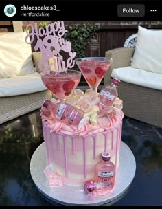 a cake with pink icing and two martini glasses on top, sitting on a table